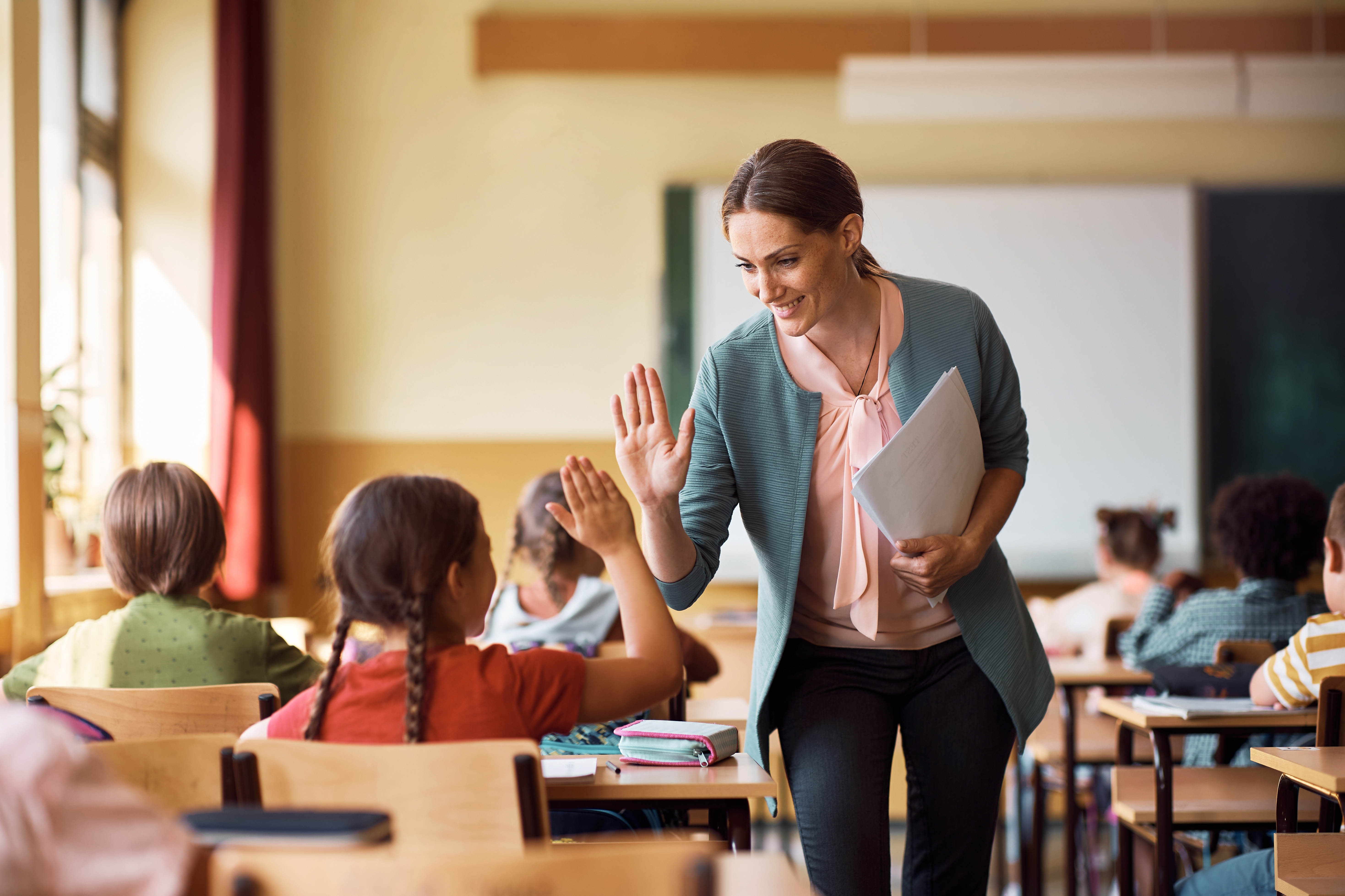 Young female student high fiving with female teacher in the classroom Young female student high fiving with female teacher in the classroom